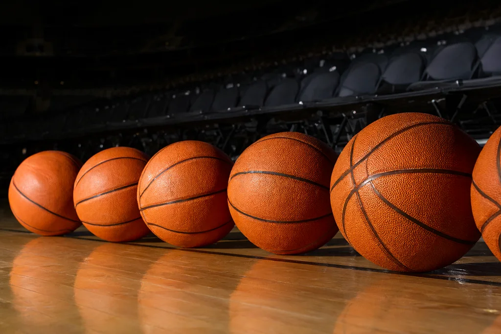 Parke zemin üzerinde yan yana dizilmiş turuncu basketbol topları, salon ışığı
