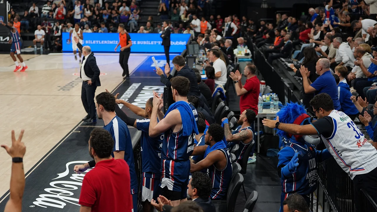 Basketbol maçında potaya atış anı, arkada tribünler ve skorboard